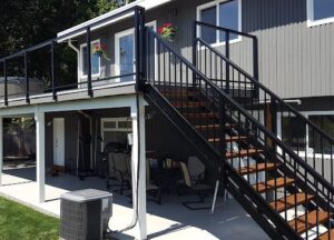 Two-story house with a black metal staircase and railing, a covered patio area below, and two flower boxes on the upper deck railing.
