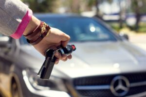 A person holds a Mercedes-Benz car key fob in front of a silver Mercedes-Benz vehicle, with the car logo visible on the grille.