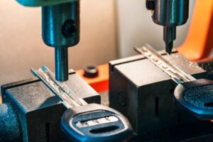 Close-up of a key cutting machine duplicating a key, with two keys held in place by metal clamps—showcasing precise Key Duplication Services and advanced cutting tools above them.