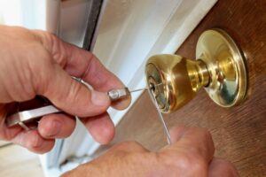 A person uses lockpicking tools to open a gold-colored door lock.