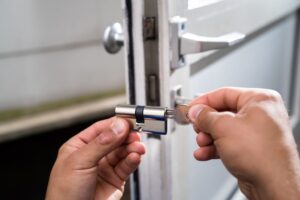 A person inserts a key into a new door lock cylinder while holding the lock in front of an open door.